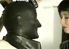 Dominant slut in latex corset provides crucified dude with a blowjob